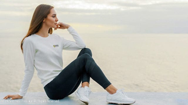 Woman sitting on a ledge in a white crew neck sweatshirt, handmade by Utmost Province.