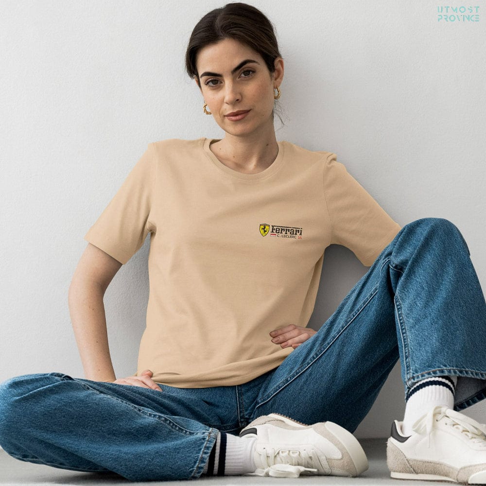 Woman wearing a beige t-shirt with a Charles Leclerc Ferrari-inspired logo and blue jeans, sitting on the floor.