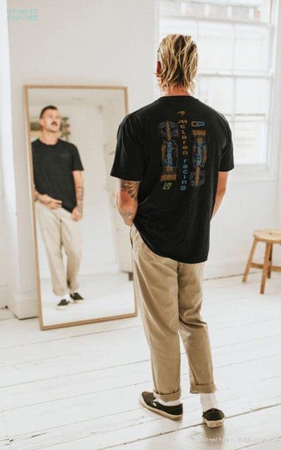 Model wearing a Mclaren F1 shirt looking into a mirror, showcasing the Utmost Province's Mclaren F1 merch collection.