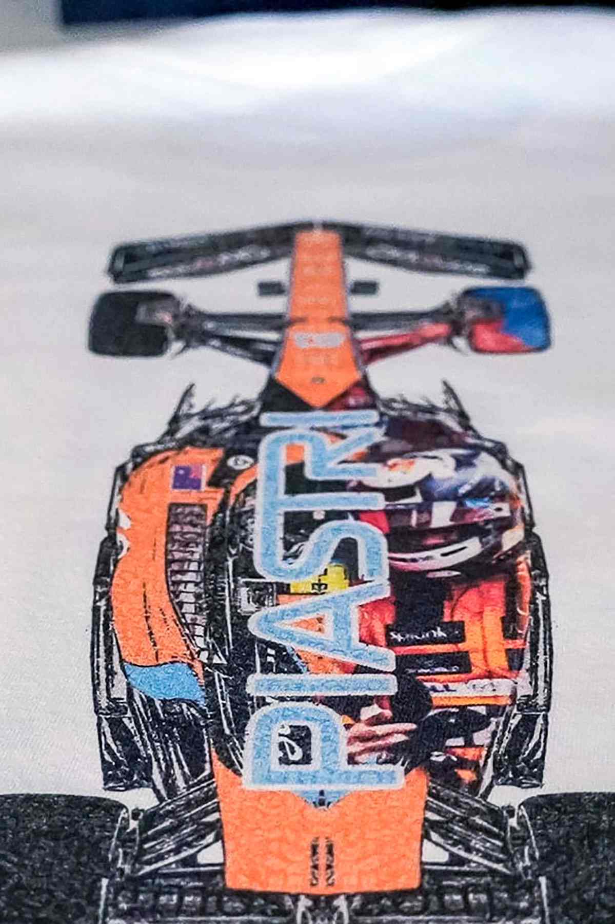 Utmost Province Oscar Piastri inspired race car t shirt laid flat on a table, highlighting the graphic design on the back of the Mclaren F1 merch.